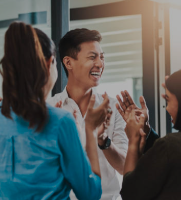 Group of colleagues smiling and clapping together in a bright office setting
