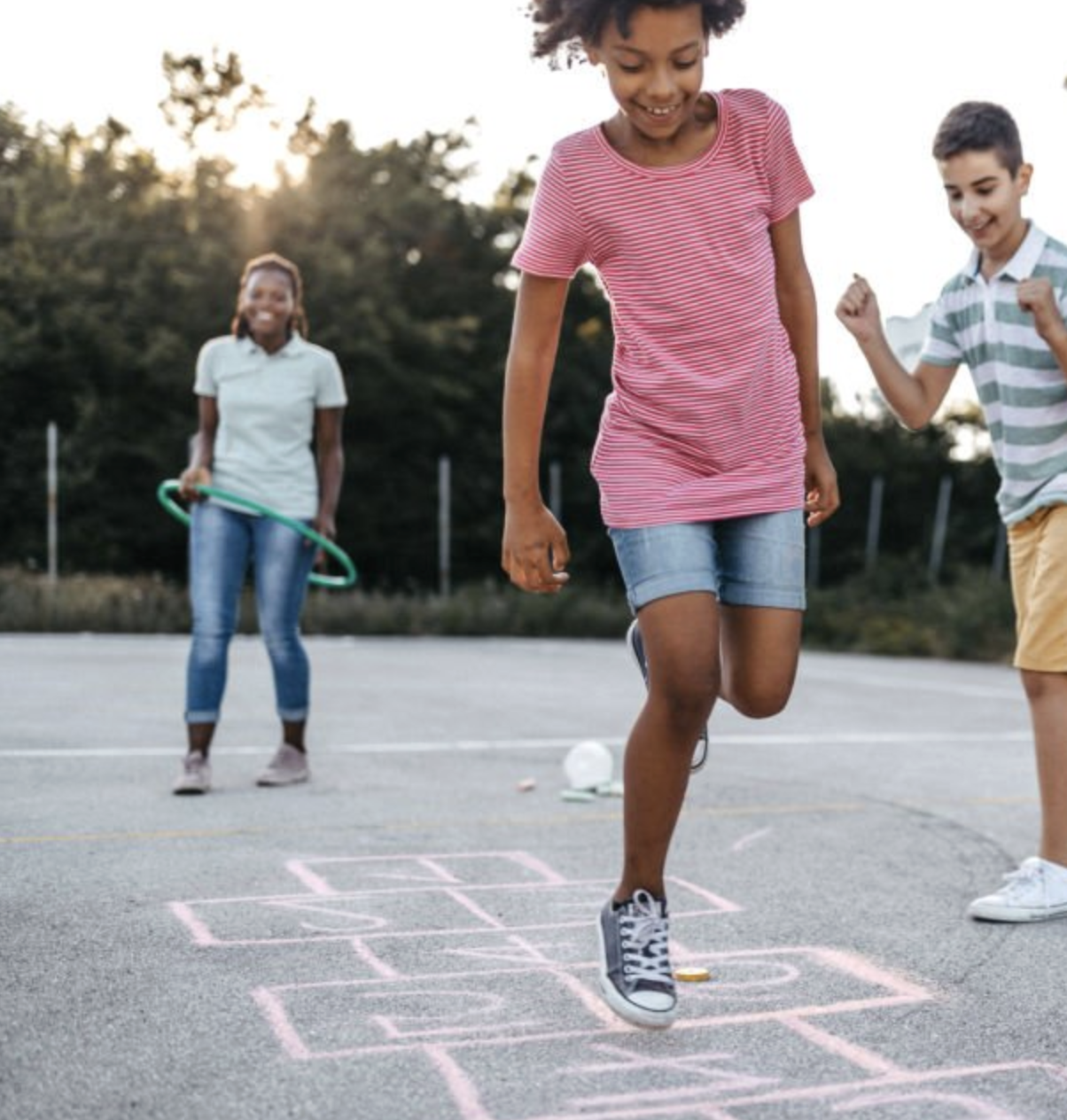 Children playing hopscotch outdoors, smiling and interacting while participating in a group activity.