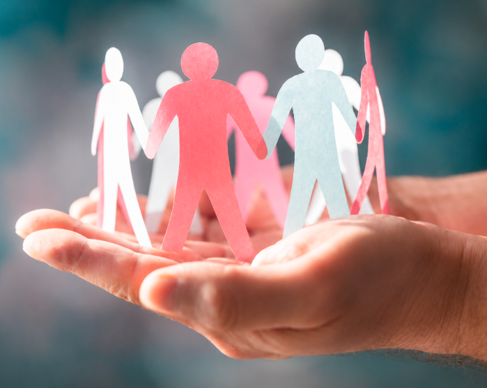 Paper-cut figures standing together in a person’s hands, representing community support, care, and connection.