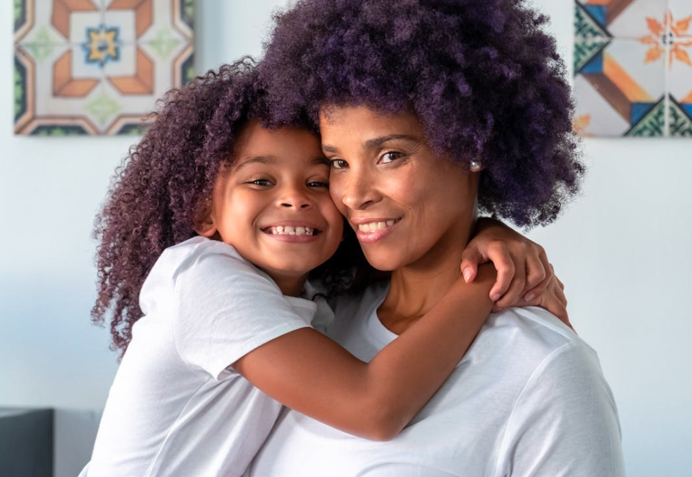 A smiling child hugs their parent while both look at the camera, expressing warmth, support, and family connection.