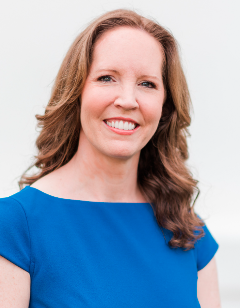 Professional headshot of Dr. Danielle Dick, a behavioral geneticist, smiling and wearing a blue dress against a light background.