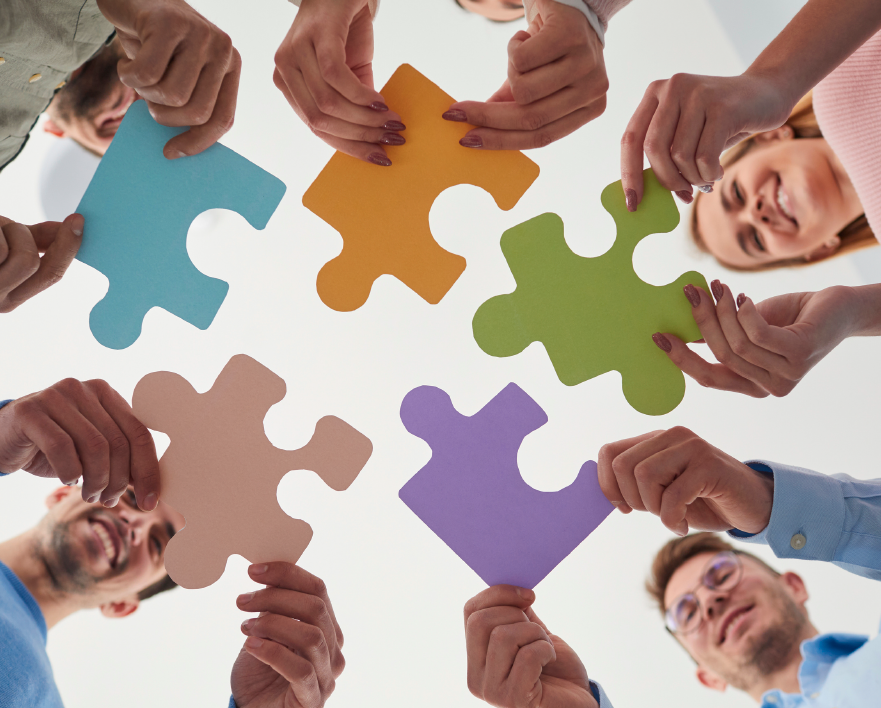 Several people hold colorful puzzle pieces in a circle, symbolizing teamwork, collaboration, and connection.