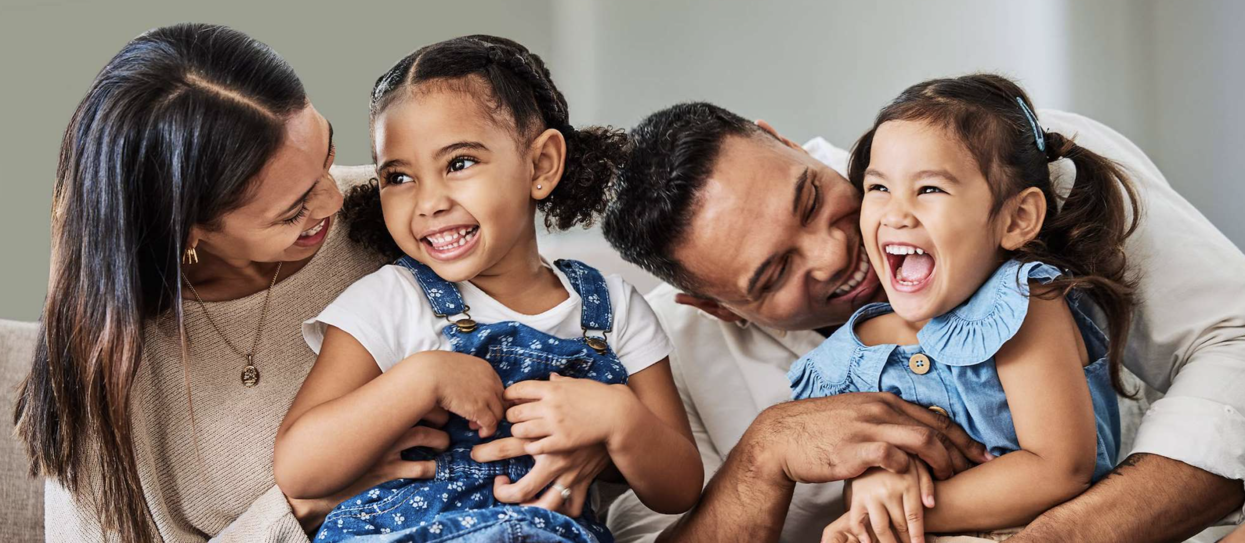 Two parents laugh and play with two young children while sitting together at home.
