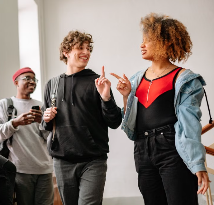 Three young adults smiling and talking together while walking indoors.