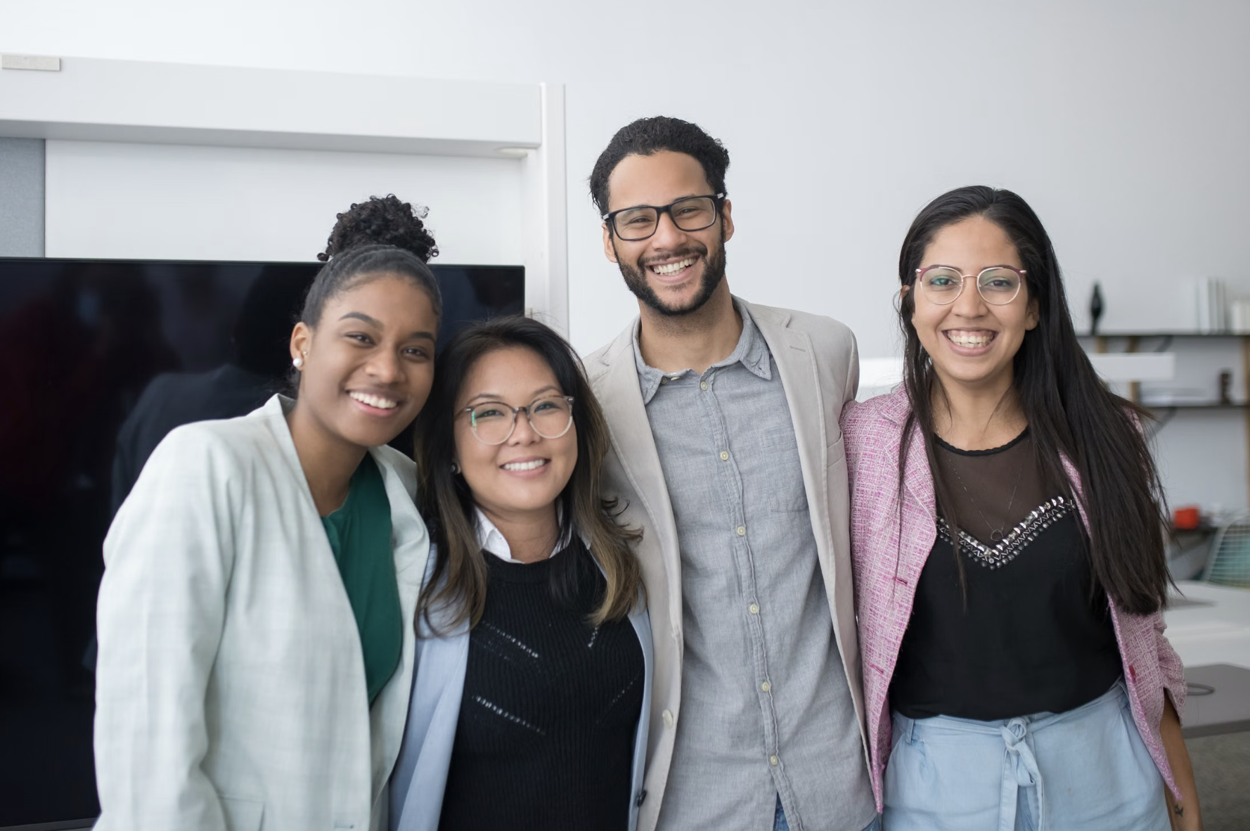 Four members of a training team stand together smiling in a bright office, representing collaboration, professionalism, and a supportive learning environment.
