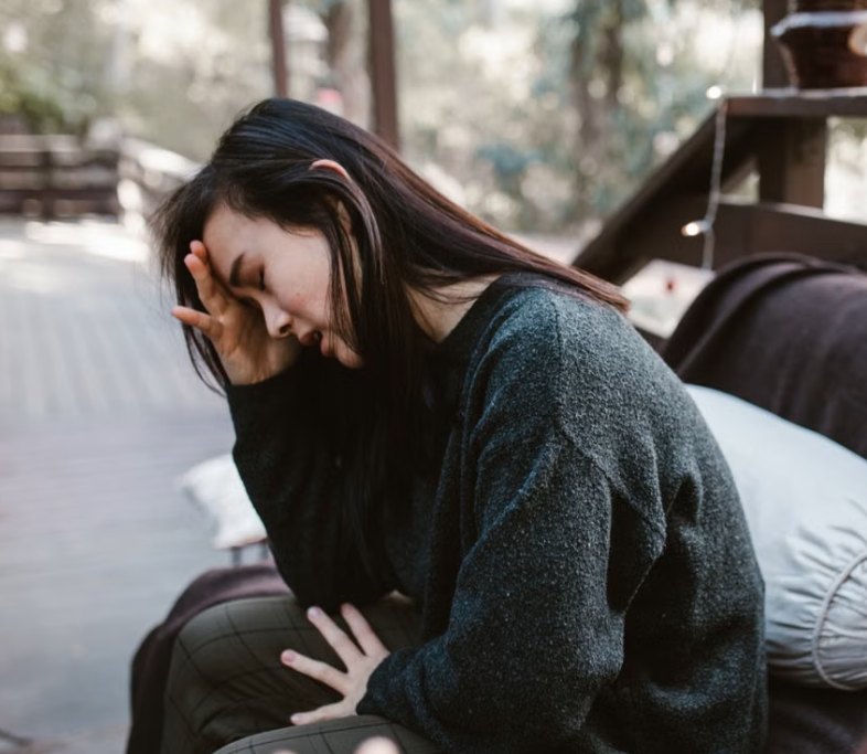 Woman sits with her head resting in her hand, appearing distressed or overwhelmed.