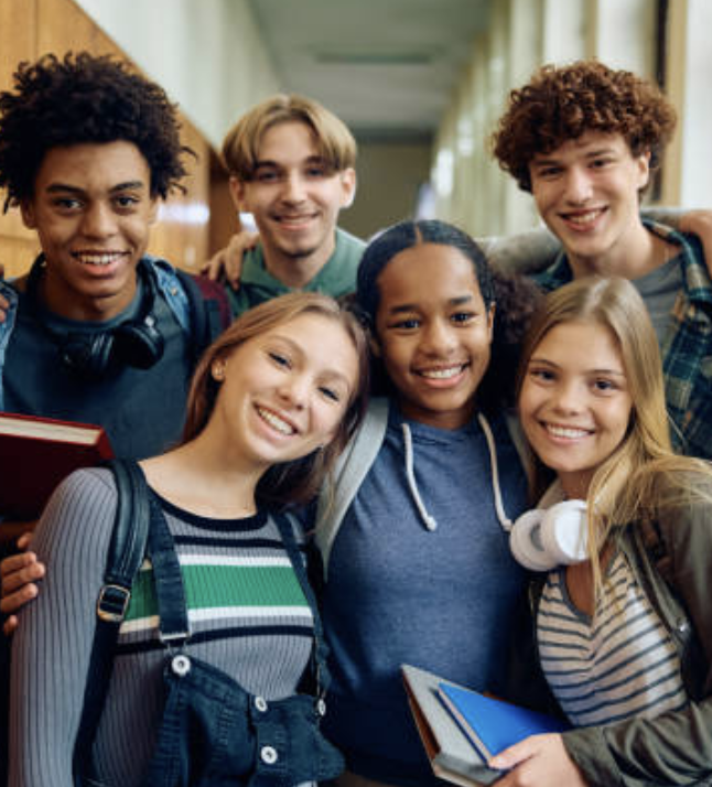 Group of smiling students with backpacks and books standing together in a school hallway.