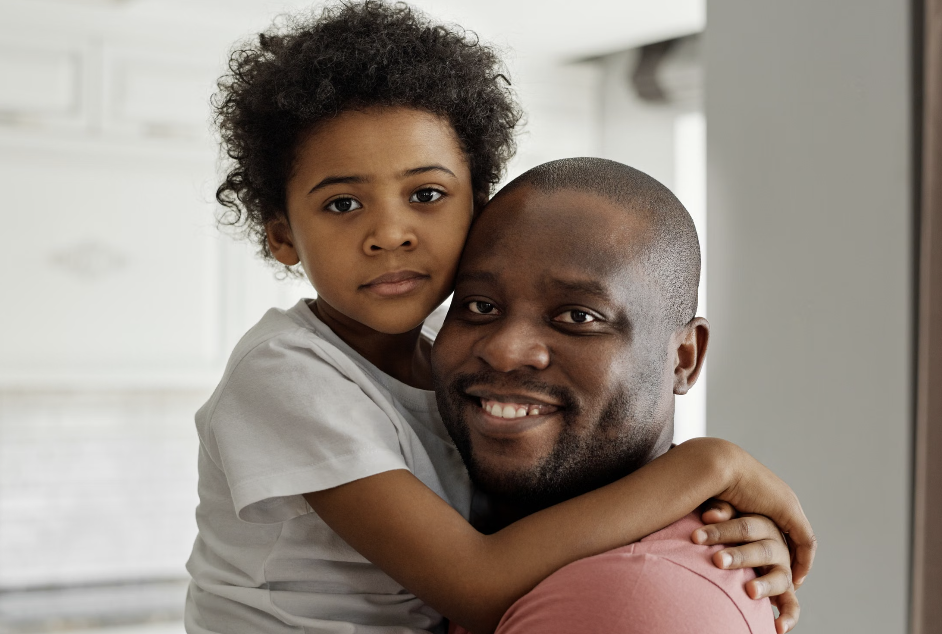 Smiling father holds his young daughter as she wraps her arms around his shoulders.