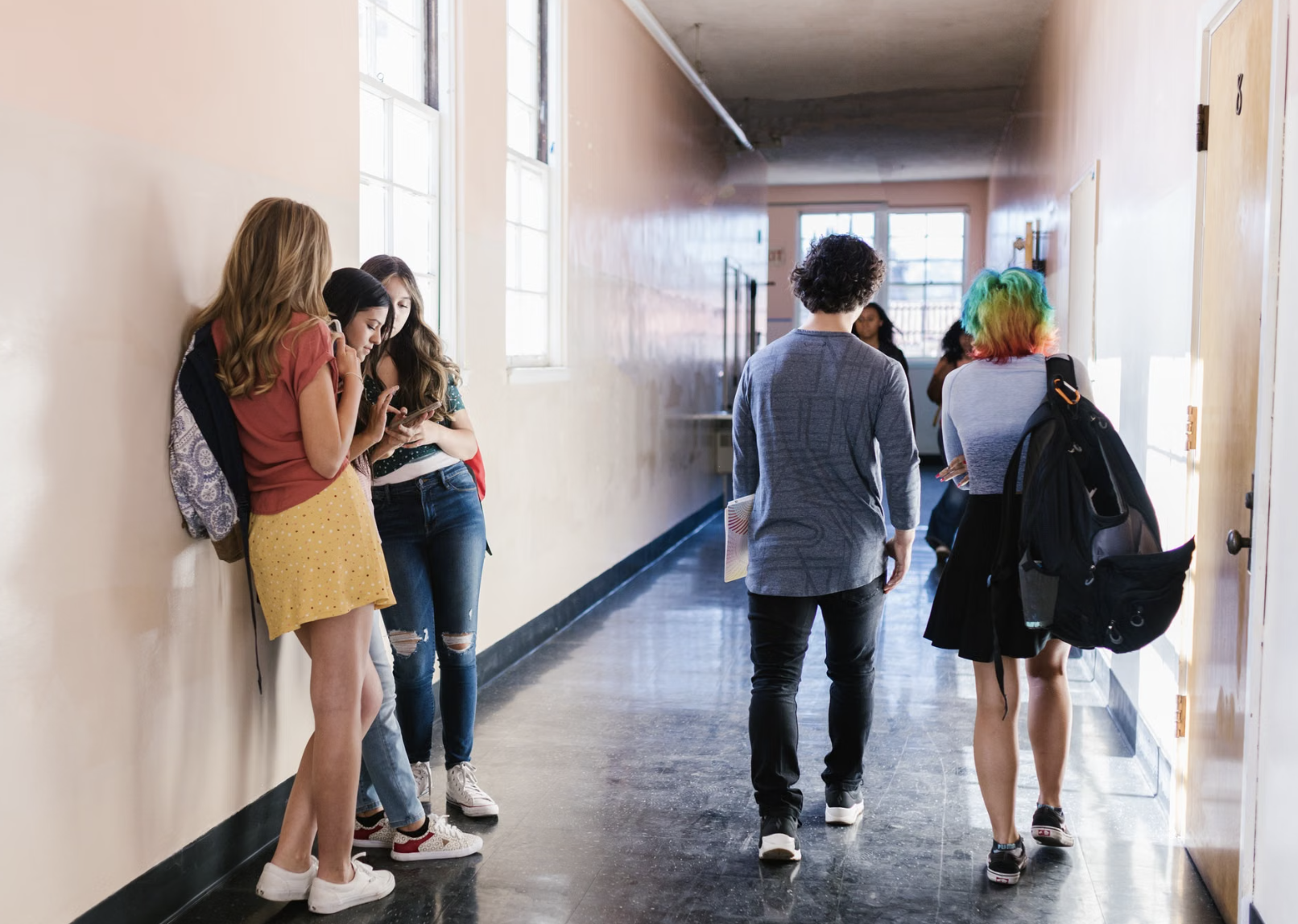Students gather and walk through a bright school hallway carrying backpacks and school materials.