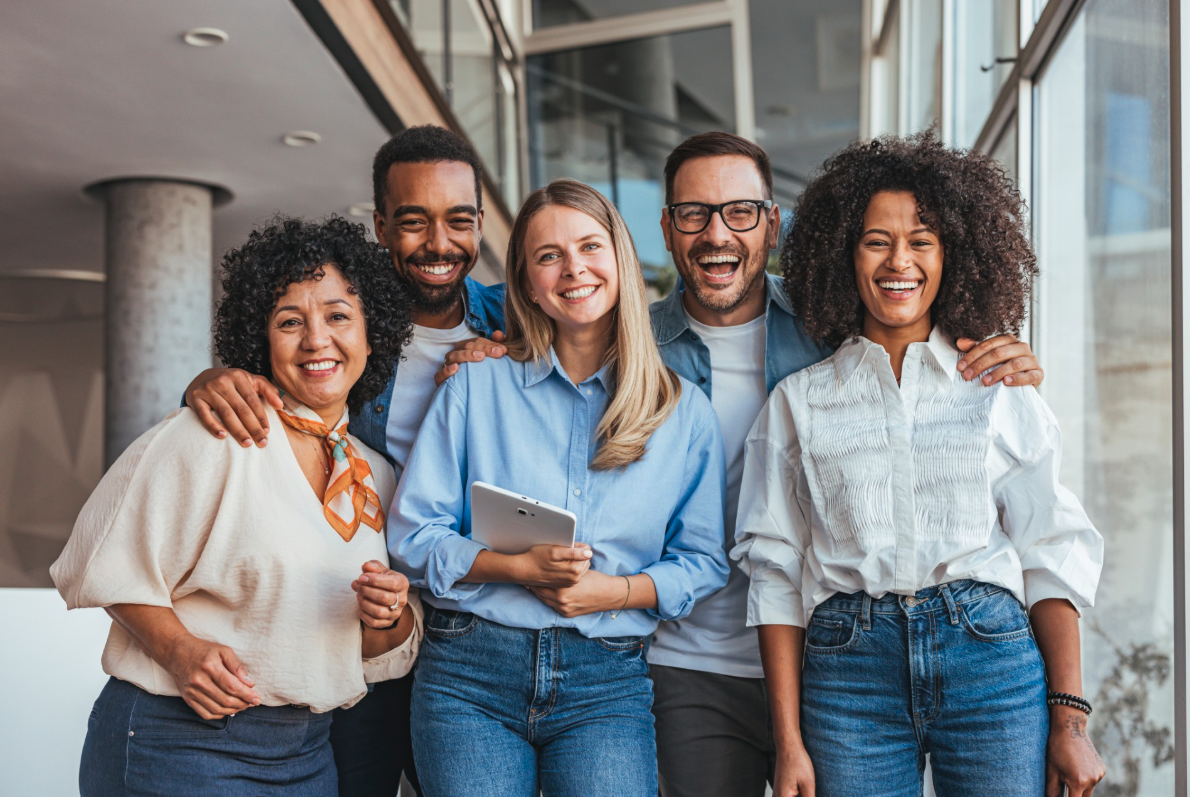 Five smiling colleagues standing together in a bright workplace.