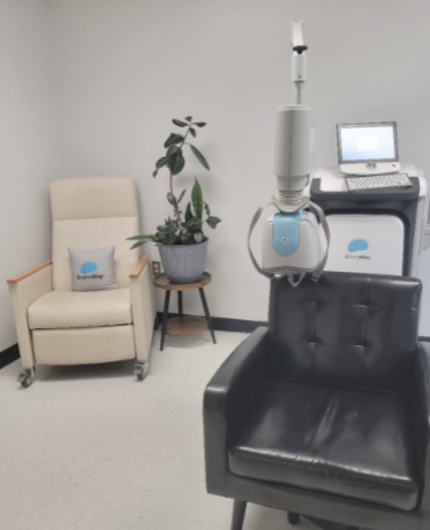 Man seated in a chair receiving a noninvasive brain stimulation treatment while a clinician operates the treatment equipment nearby.