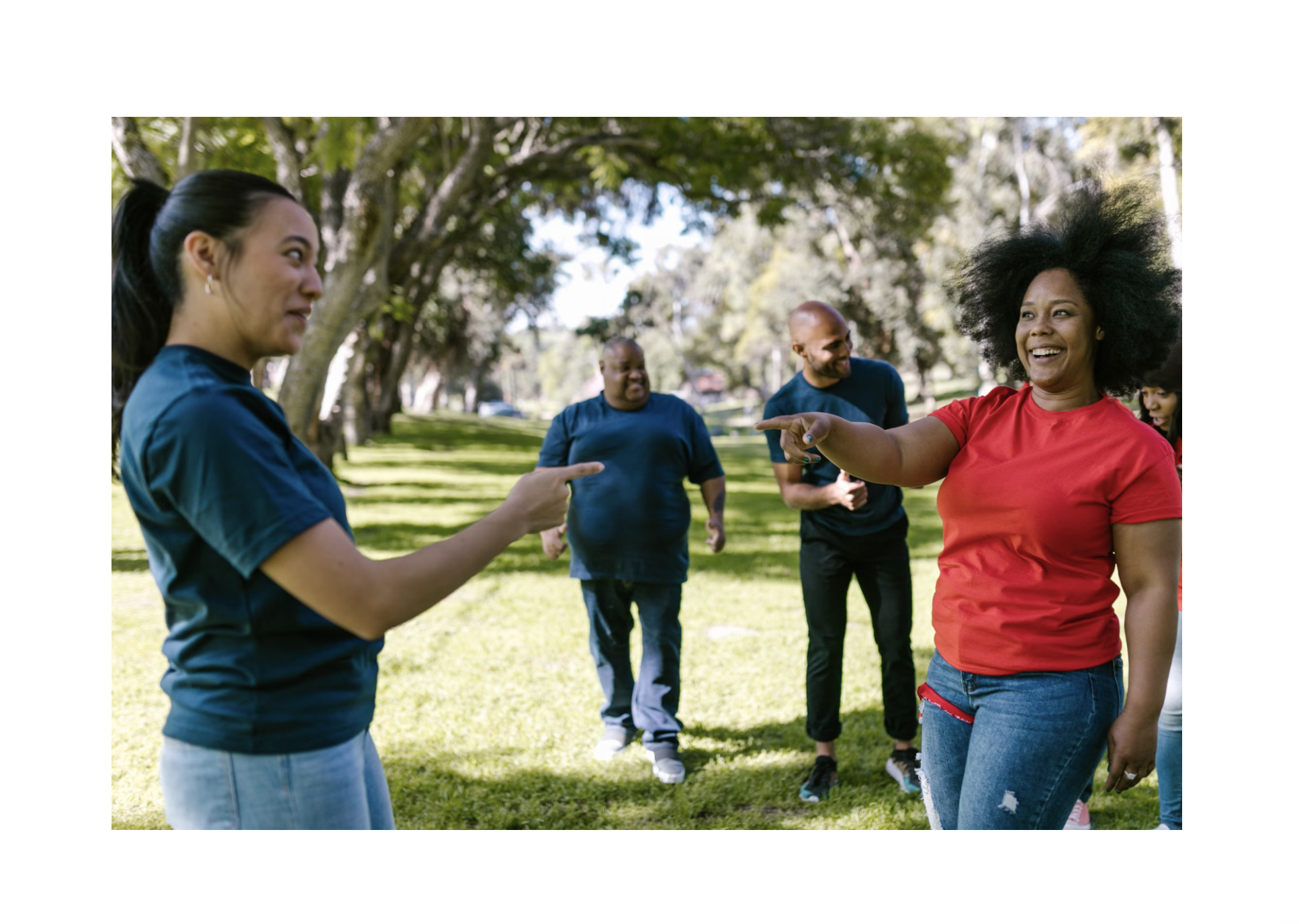 Diverse group of adults smiling and interacting together outdoors in a park.
