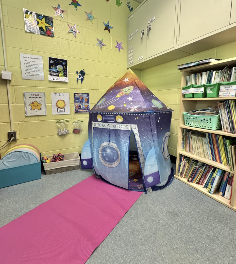 Classroom reading and activity corner with a colorful space-themed play tent, bookshelves, student artwork, and learning materials.