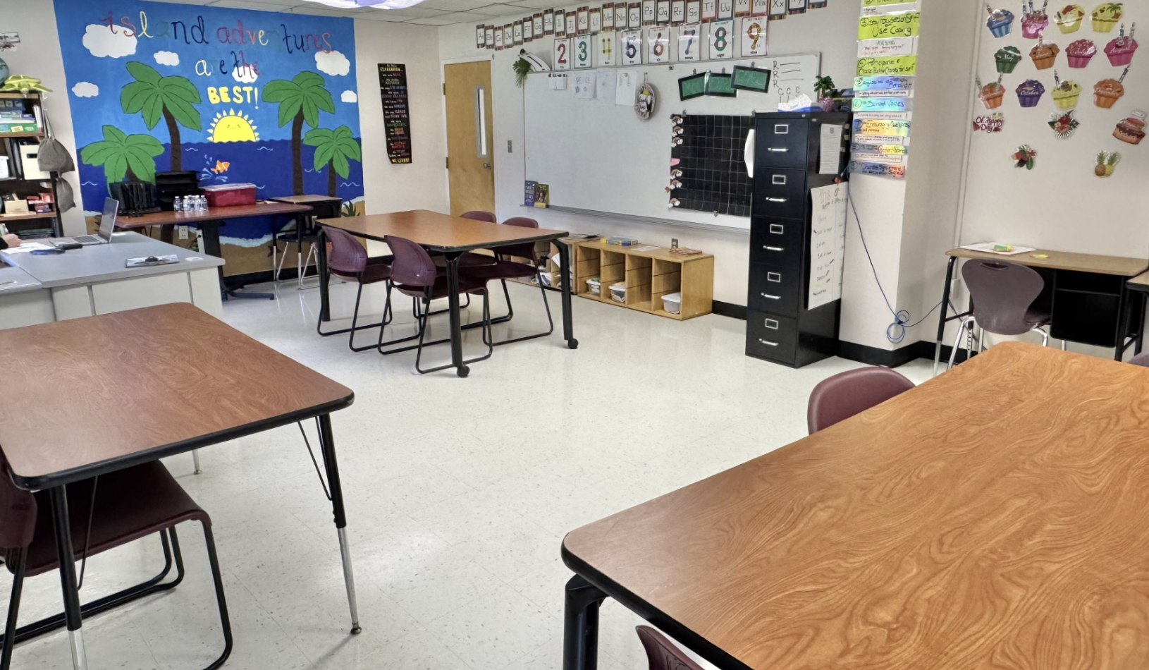 Classroom with tables, chairs, a whiteboard, educational displays, and a colorful island-themed bulletin board.