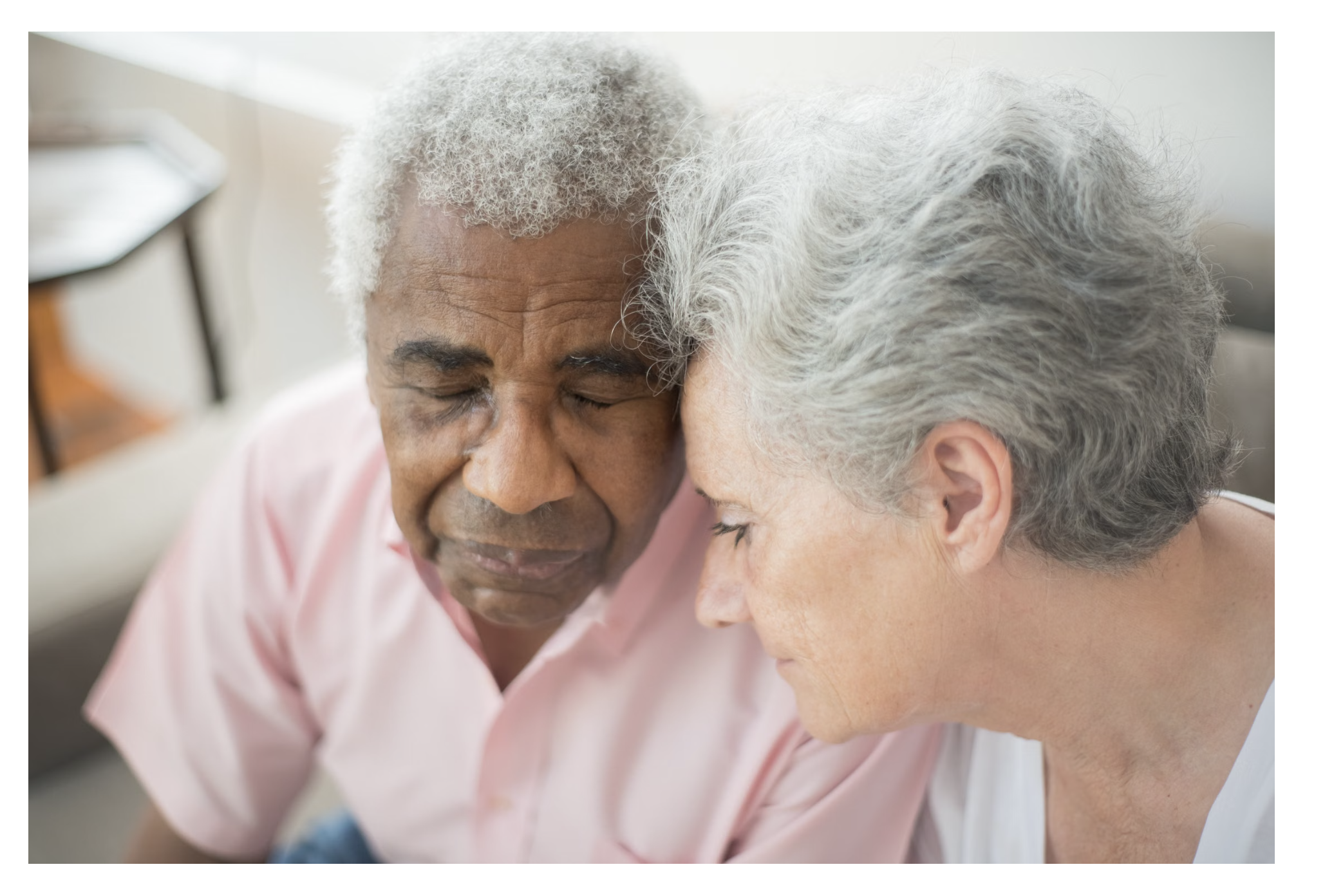 Two older adults sitting closely together and sharing a quiet, supportive moment.