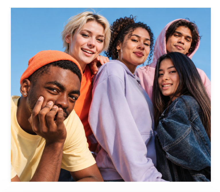 Diverse group of young adults smiling together outdoors under a blue sky.