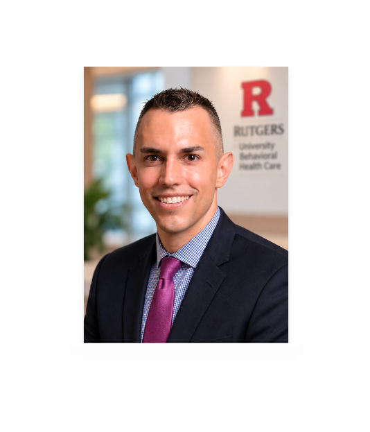 Professional photo of Dr. Keith Stowell, Chief Medical Officer with an image of Rutgers R in red on the wall that reads Rutgers University Behavioral Health Care.