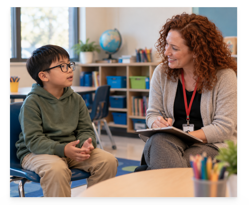 Young student with glasses talking with a mental health professional in a classroom.